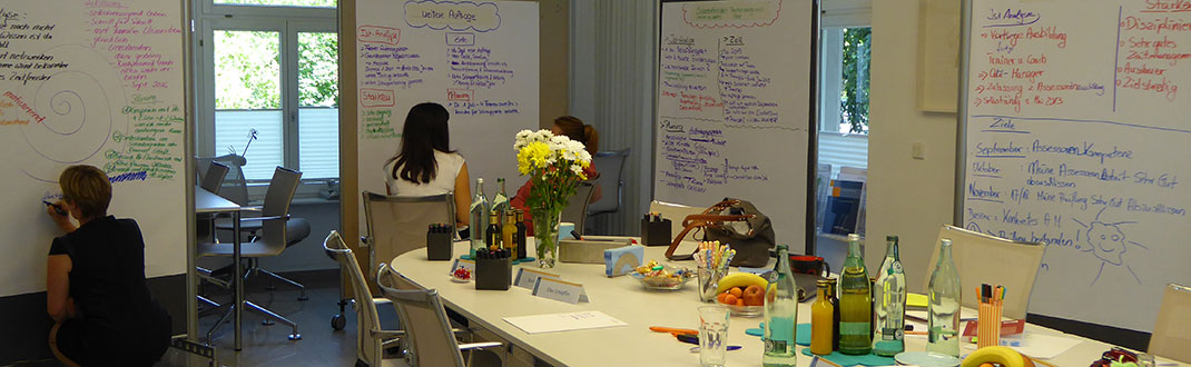 Schlungsraum mit Flipcharta und 3 adran arbeitenden Leuten; auf den Tischen Getränke und Unterlagen